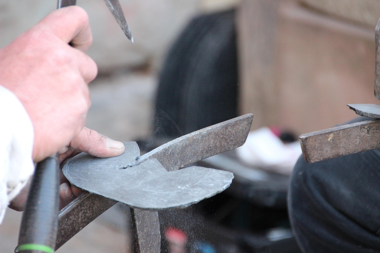 Roofer trimming a slate by hand with a slater's hammer