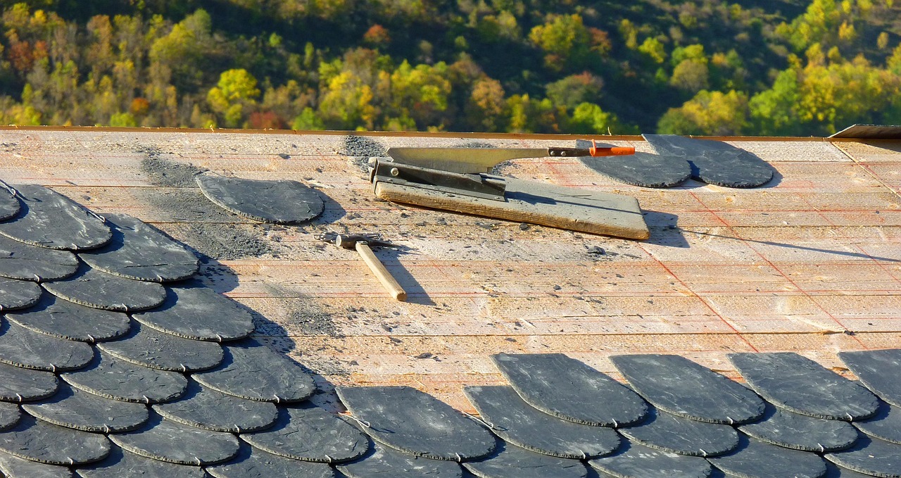 New slates being fixed on a roof, with a slate cutter and hammer